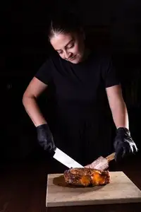 A chef uses a cleaver to carve a large cooked tomahawk steak on a wooden board in the restaurant kitchen.
