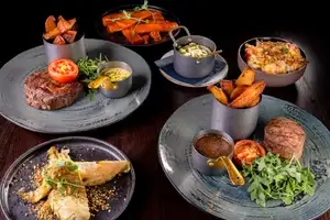 Fillet and rib-eye steaks with chips, rocket, roasted tomatoes and sauces sit among bowls of Hispi cabbage, carrots and another side dish.