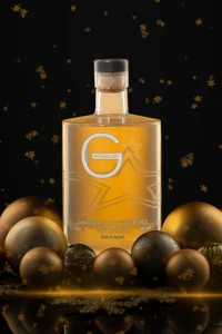 The amber liqueur bottle is centred on a dark reflective surface, surrounded by metallic baubles and scattered gold decoration.