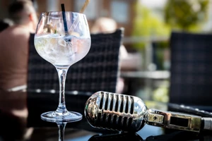 The drink and microphone are set on an outdoor table, with diners and greenery softly blurred behind them during the I'll Remember You gin launch.