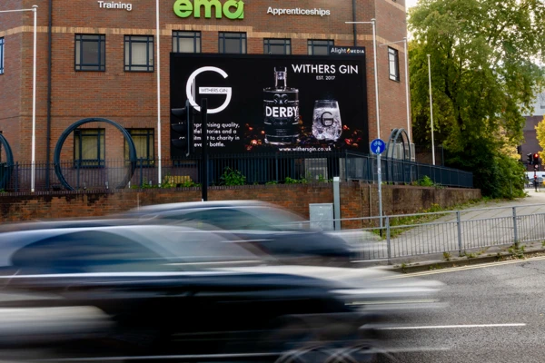 A 6 m by 3 m roadside billboard displays a Withers Derby Gin bottle and branded glass on a brick building, with motion-blurred cars passing in front.