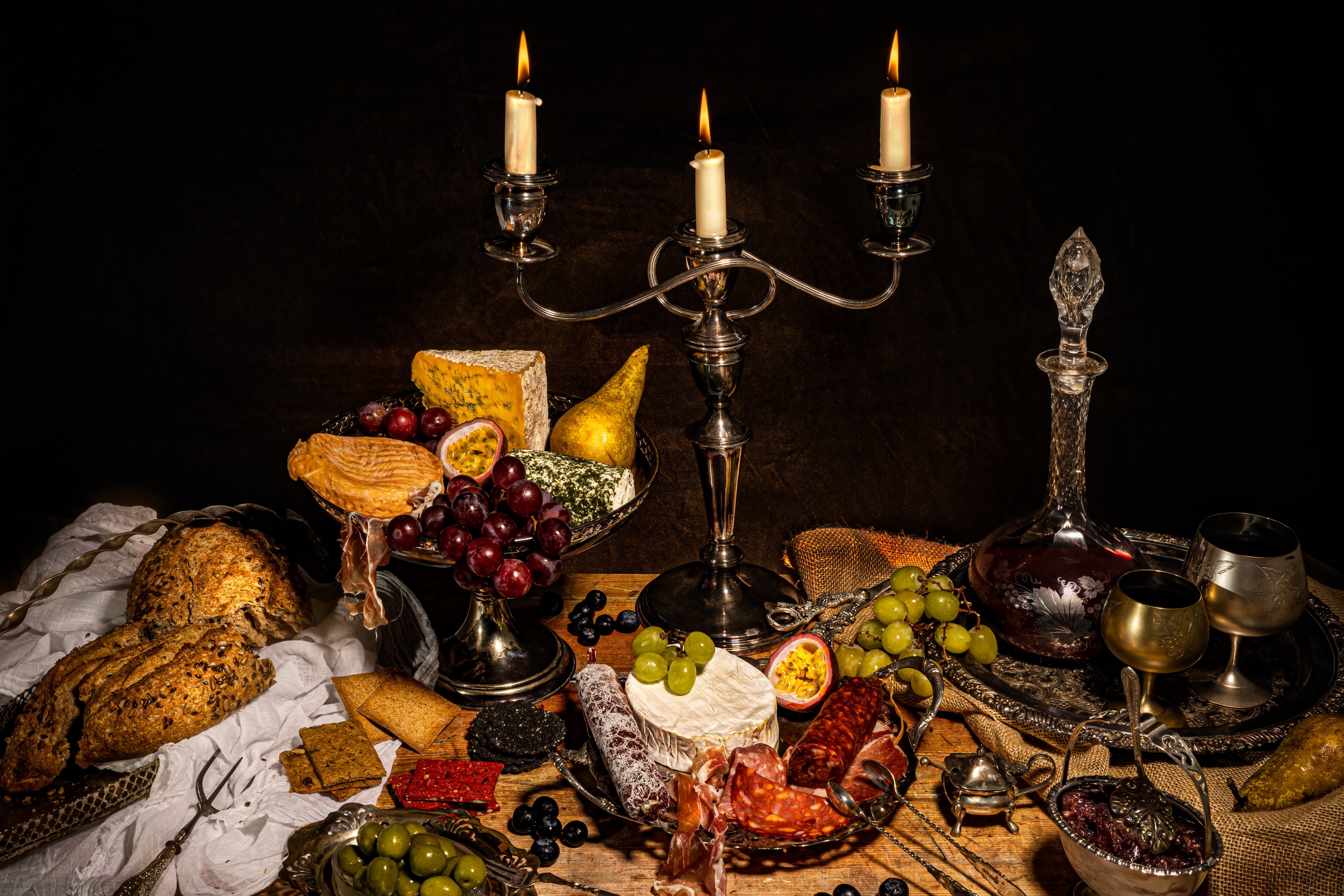 Creative photograph of a spread of cheese, wine and charcuterie. Dramatically photographed like a medieval feast, by JaxMore Food and Drink Photography, in their Derby studio.