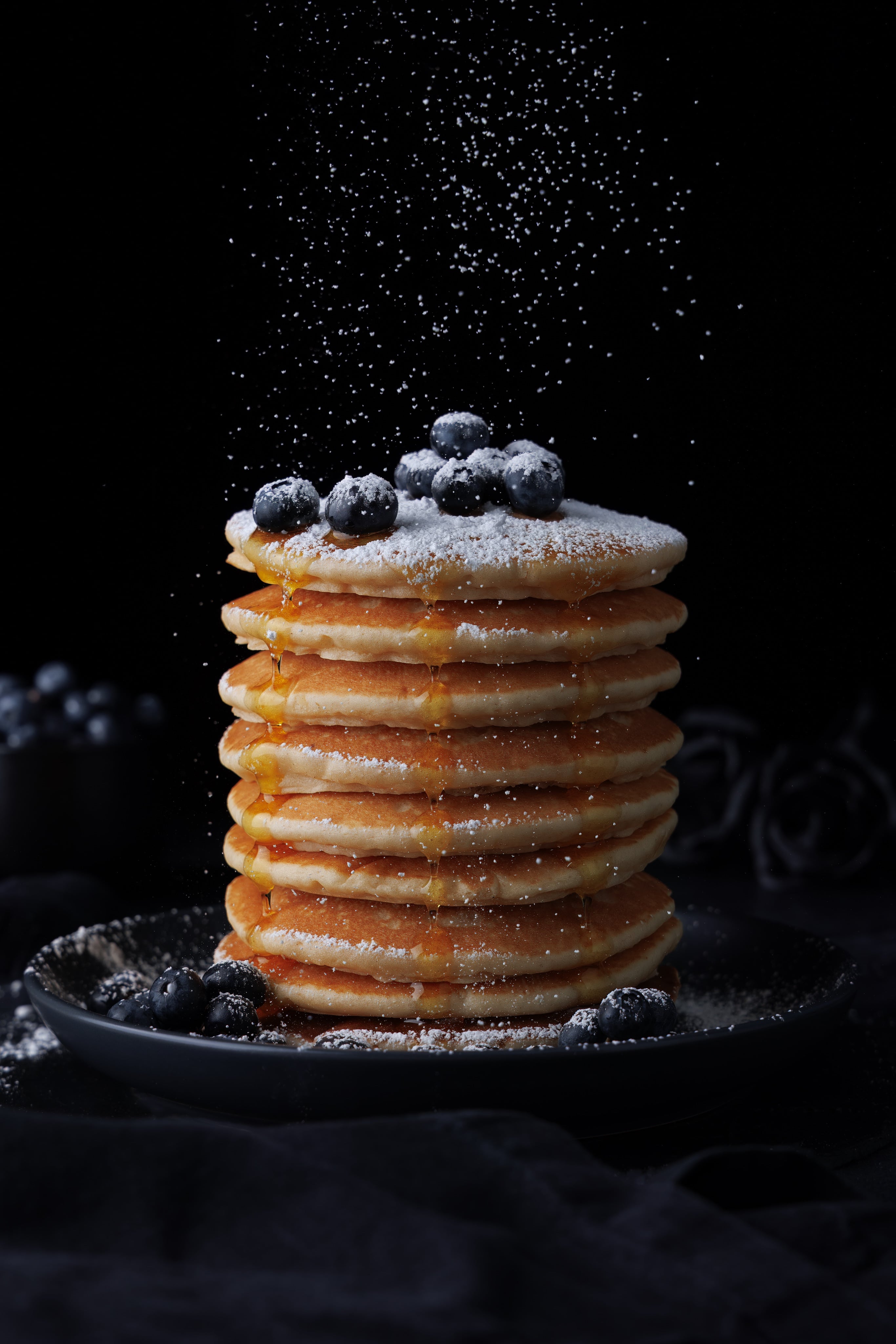 Pancake stack with blueberries, syrup and sugar, in a dark and moody style. Creative Dessert Photography by JaxMore Food and Drink Photography, in their Derby studio.