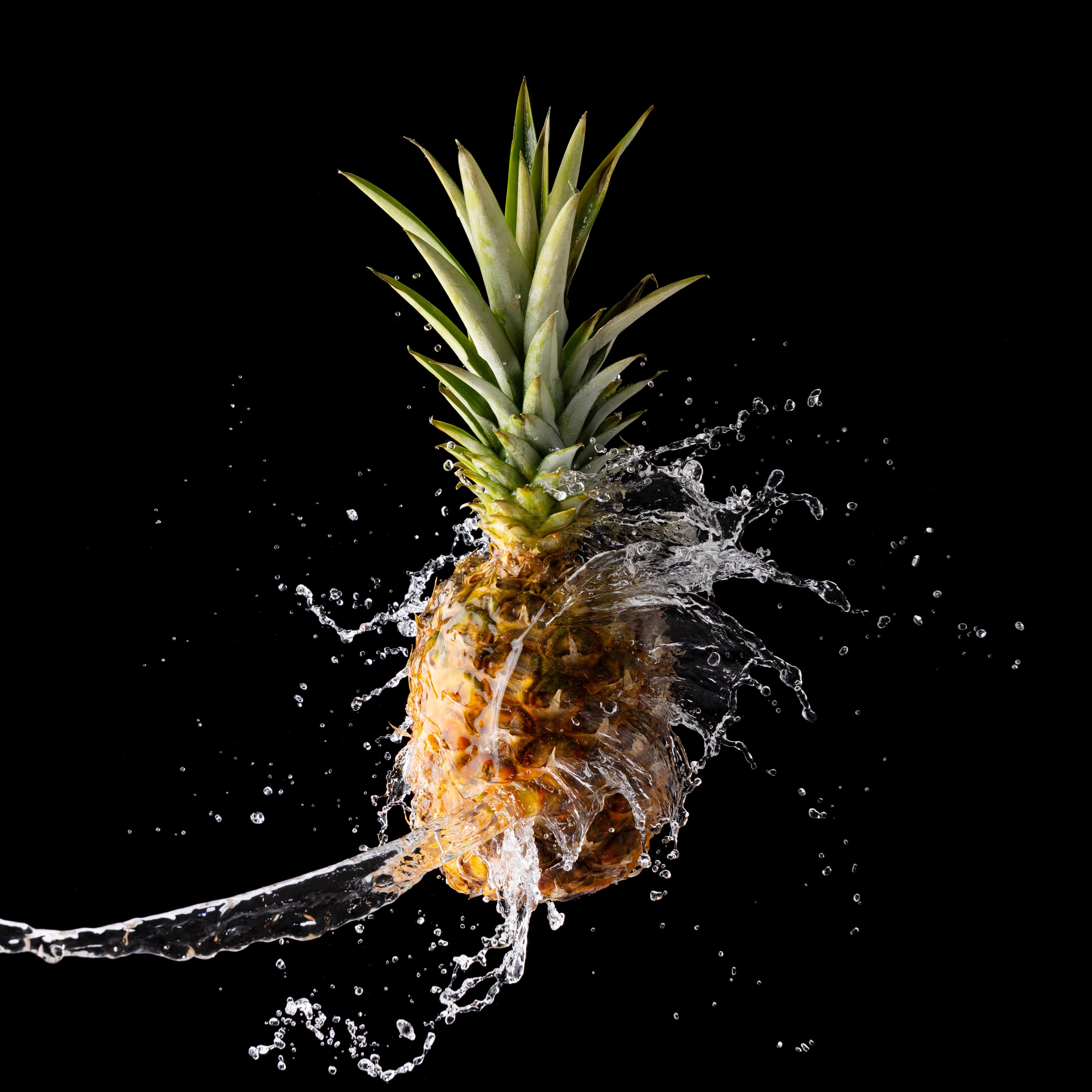 A wave of water hits a pineapple, to illustrate how juicy it is! A creative splash photograph by JaxMore Food and Drink Photography, shot in their Derby studio.